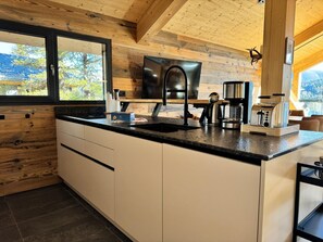 Une cuisine moderne dotée d’un grand îlot central, d’appareils électroménagers intégrés et offrant une vue sur l’extérieur.