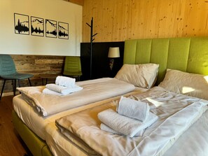 Een hotelkamer met twee bedden, een groen bekleden hoofdeinde, een houten wand en een stoel.