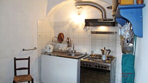 Ett kompakt kök med vita skåp, en spis, ett handfat och en trästol.