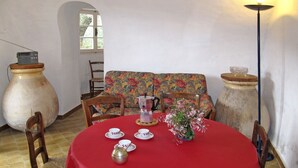 En matplats med ett runt bord täckt av en röd duk, omgivet av trästolar. En blommönstrad soffa står längs väggen, och en stor vas med blommor står på bordet.