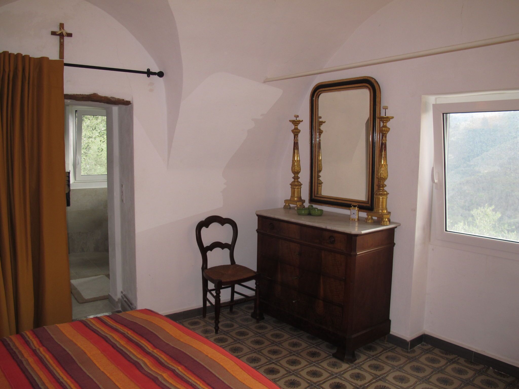 Une chambre à coucher avec un lit, une commode en bois, une chaise, un miroir et une fenêtre.
