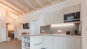 A modern kitchen with white cabinetry, a built-in microwave, and a coffee maker. - Das Georgen, Großglockner+Kitzsteinhorn by Interhome (Bruck)