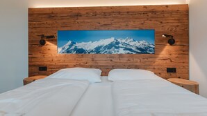 Una cama doble con sábanas blancas en una habitación con paneles de madera y un cuadro grande de un paisaje montañoso.
