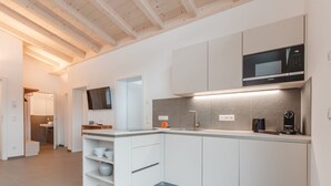 A modern kitchen with white cabinetry, a built-in microwave, and a coffee maker. - Das Georgen, Kitzsteinhorn by Interhome (Bruck)