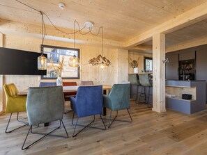 A modern interior with a wooden ceiling, a dining area with colorful chairs, and a kitchen area.