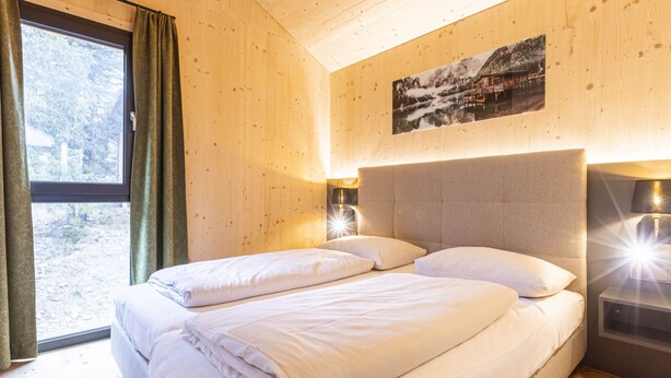 Un dormitorio con cama, ventana con cortinas, un cuadro en la pared y lámparas de noche.