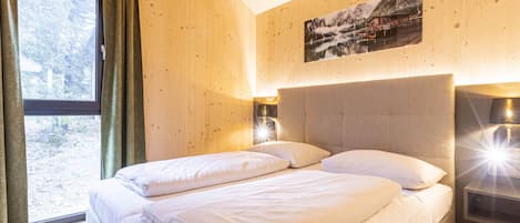 A bedroom with a bed, a window with curtains, a wall-mounted picture, and bedside lamps.