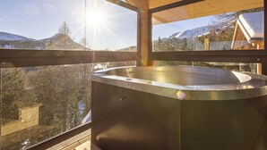 Un jacuzzi en una cabaña de madera con vista a montañas nevadas.
