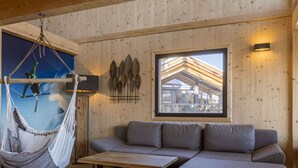 Una habitación acogedora con una hamaca, un sofá, una mesita de centro y un ventanal con vistas a un edificio.