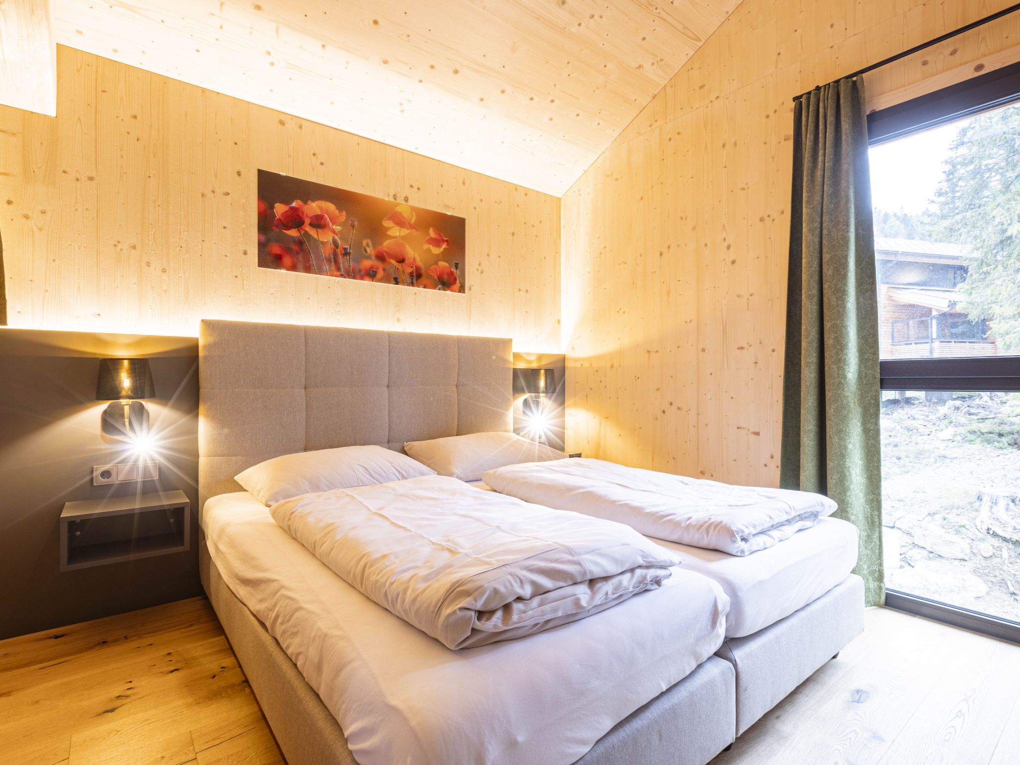 A bedroom with a bed, bedside lamps, a painting, and a window with curtains.