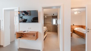 A modern hotel room with a wooden bed, a TV mounted on the wall, and a wooden cabinet with a remote control.