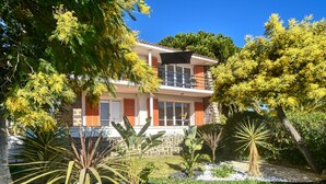 Ein zweistöckiges Haus mit Balkon, umgeben von Pflanzen und Bäumen.