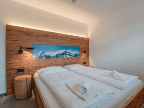 A modern hotel room with a wooden headboard, a large mountain painting, a bed with white linens, and a wooden nightstand. - Das Georgen, Maiskogel by Interhome (Bruck)