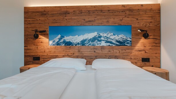 A double bed with white linens in a room with wooden paneling and a large mountain landscape painting above it. - Das Georgen, Maiskogel by Interhome (Bruck)