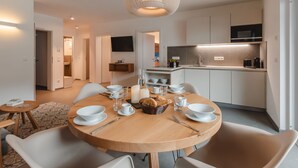 A modern kitchen with white cabinets, a built-in oven, and a microwave. There is a dining area with a round wooden table, white chairs, and a hanging light fixture. - Das Georgen, Maiskogel by Interhome (Bruck)