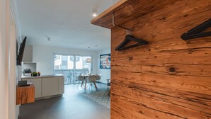 A modern kitchen with a wooden accent wall, a dining area with a table and chairs, and a view through a glass door to the outside. - Das Georgen, Maiskogel by Interhome (Bruck)