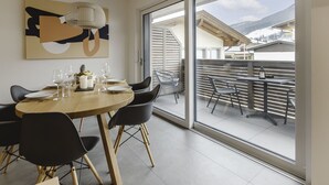 A dining area with a wooden table and black chairs, a hanging light fixture, and a large window with a view of mountains.