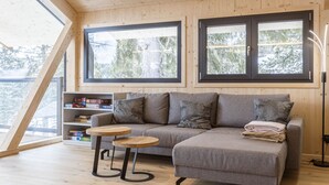 Un salón acogedor con un sofá gris, dos mesas redondas de madera y una estantería llena de juegos de mesa.
