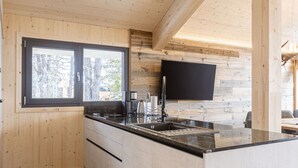 Una cocina moderna con armarios de madera, encimera negra y ventana con vistas a un paisaje nevado.