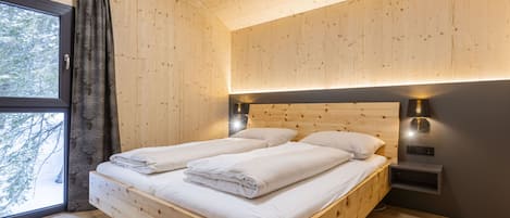 Een houten slaapkamer met een bed, gordijnen en een nachtkastje.