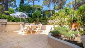 Eine Terrasse mit Tisch und Stühlen, umgeben von verschiedenen Pflanzen und Bäumen.