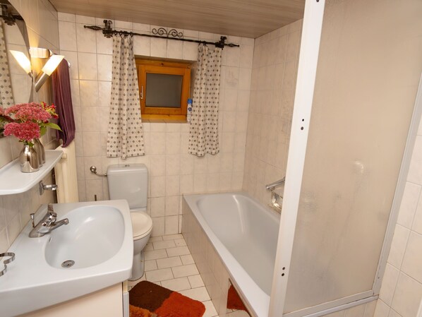 A bathroom with a toilet, sink, bathtub, and a window with patterned curtains.