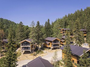 Un ensemble de chalets en bois dotés de balcons, entourés d’une forêt dense, ce qui suggère un lieu d’hébergement isolé, propice à la communion avec la nature.