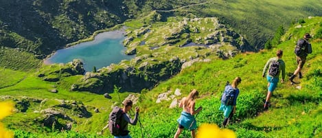 A group of hikers on a grassy mountain trail with a lake in the background.