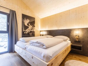 A wooden room with a bed, a window with curtains, a wall-mounted lamp, and a framed picture. - 02_NTH024_Sup Chalet mit Sauna und Hot Tub 2 Etage by Interhome (Turracher Höhe)