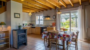 A kitchen with wooden beams, a dining table with a colorful tablecloth, and a view of the outdoors through large windows.