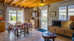 A cozy living room with wooden beams, a dining area with a table and chairs, a television, and a fireplace.