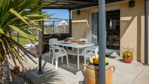 A covered patio with a table and chairs, potted plants, and a view of the neighborhood.