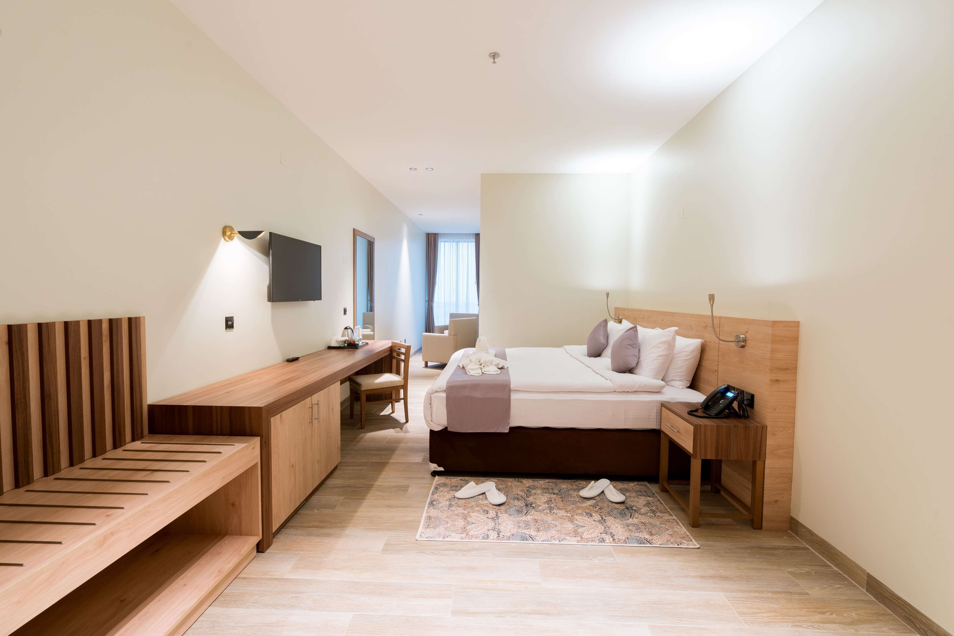 A modern hotel room with a wooden bed, a desk, and a TV mounted on the wall.