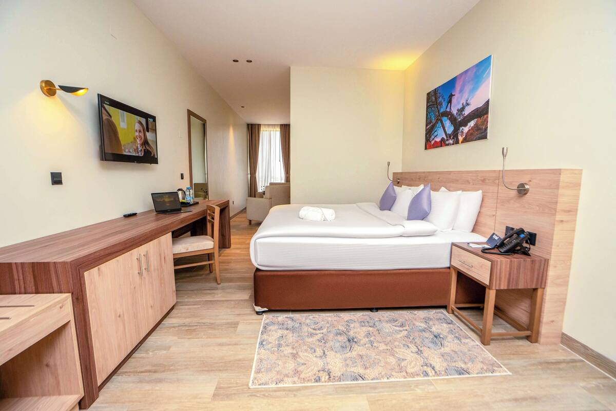A modern hotel room with a bed, desk, and a large painting on the wall.
