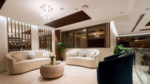 A modern living room with two sofas, a round coffee table, and a dark armchair. Large windows provide a view of the cityscape. - Kyriad Muscat (Muscat)