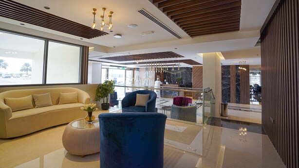 A modern lobby with a sofa, a blue armchair, a glass coffee table, and a potted plant. - Kyriad Muscat (Muscat)