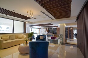 A modern lobby with a sofa, a blue armchair, a glass coffee table, and a potted plant. - Kyriad Muscat (Muscat)