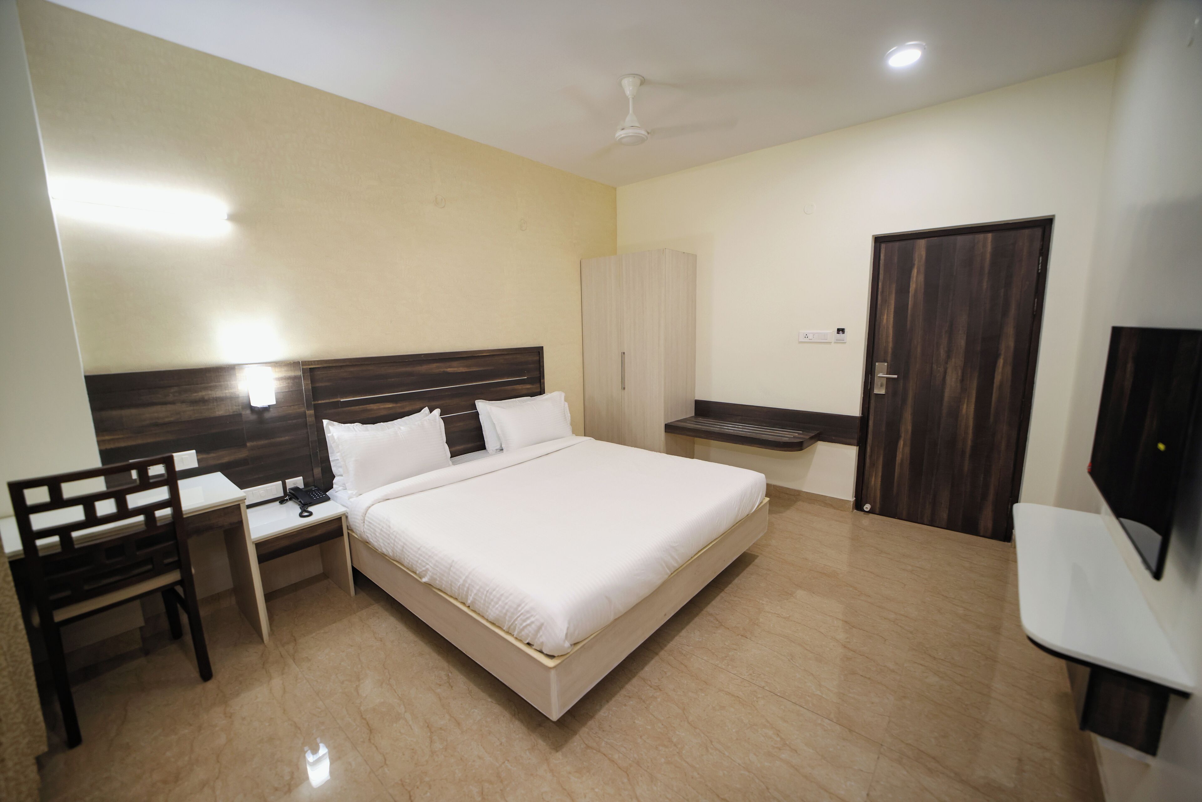 A bedroom with a bed, a desk, a chair, a wardrobe, and a television.