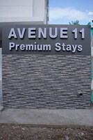 Letrero que dice "AVENUE 11 Premium Stays", con una pared texturizada y una puerta metálica.