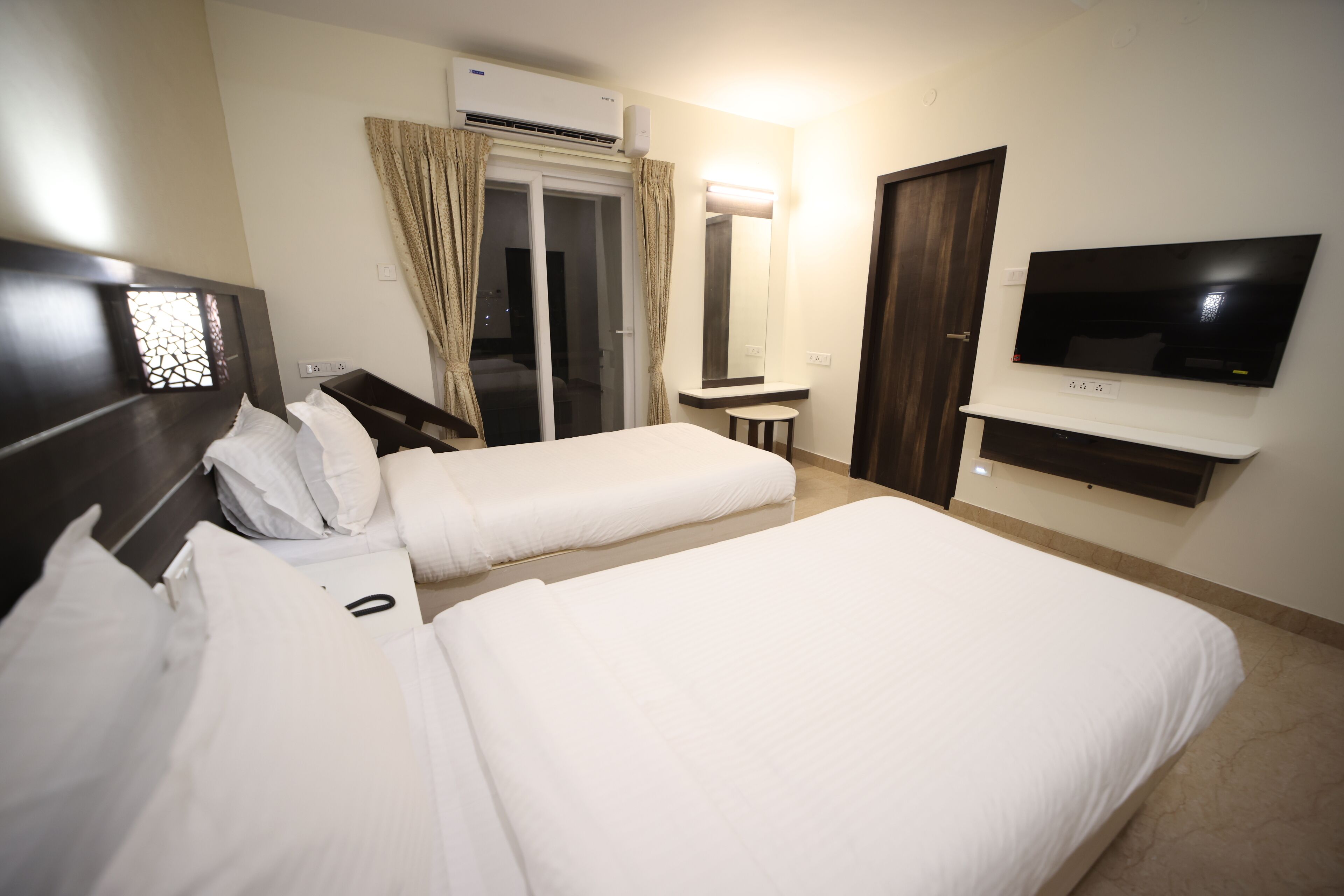 Een hotelkamer met twee bedden, een televisie, een tafeltje, een spiegel en een airconditioning.