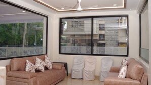 Una sala de estar moderna con dos sofás, un ventilador de techo y ventanas amplias con persianas estampadas.