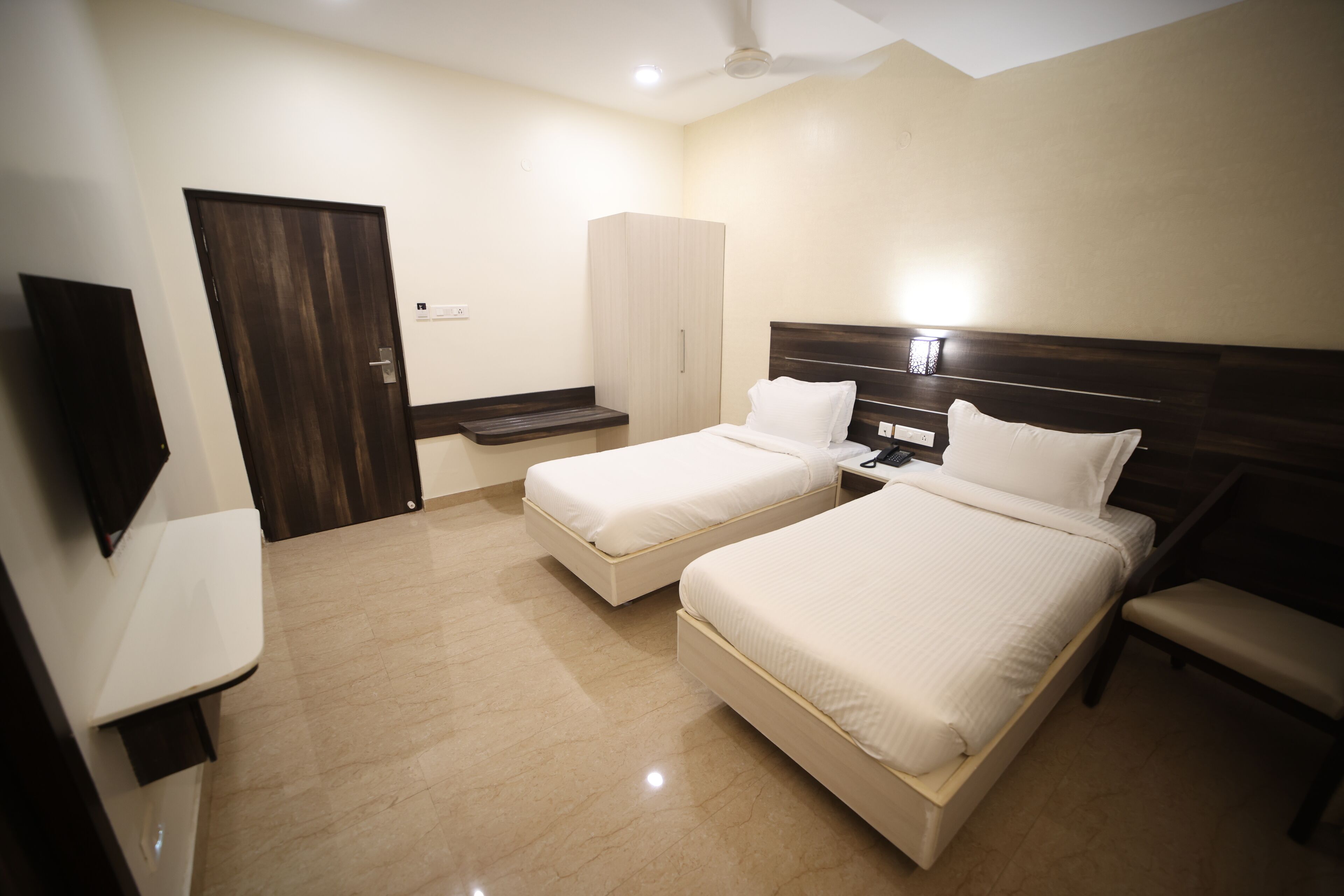 A hotel room with two beds, a wardrobe, a TV, and a bench.