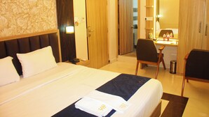 A hotel room with a large bed, a desk with a chair, a mirror, and a wardrobe. - Hotel Pavitra (Purnia)
