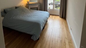 A bedroom with a bed, a nightstand, a lamp, a window with curtains, and a view of the outside. - Quite, Lovely Apartment in Paris (Paris)