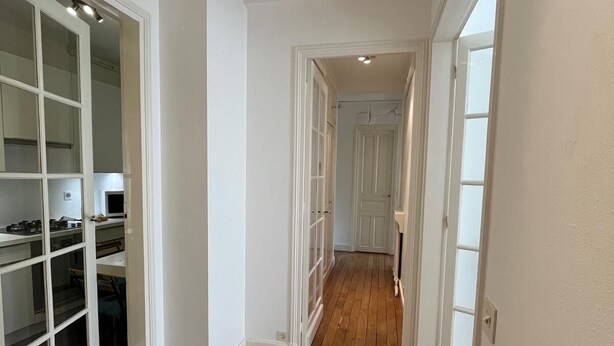 A hallway with wooden flooring and white walls, leading to a room with a large window and a door. - Quite, Lovely Apartment in Paris (Paris)