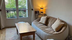 A cozy living room with a sofa, a small table, a rug, and a window with curtains. - Quite, Lovely Apartment in Paris (Paris)