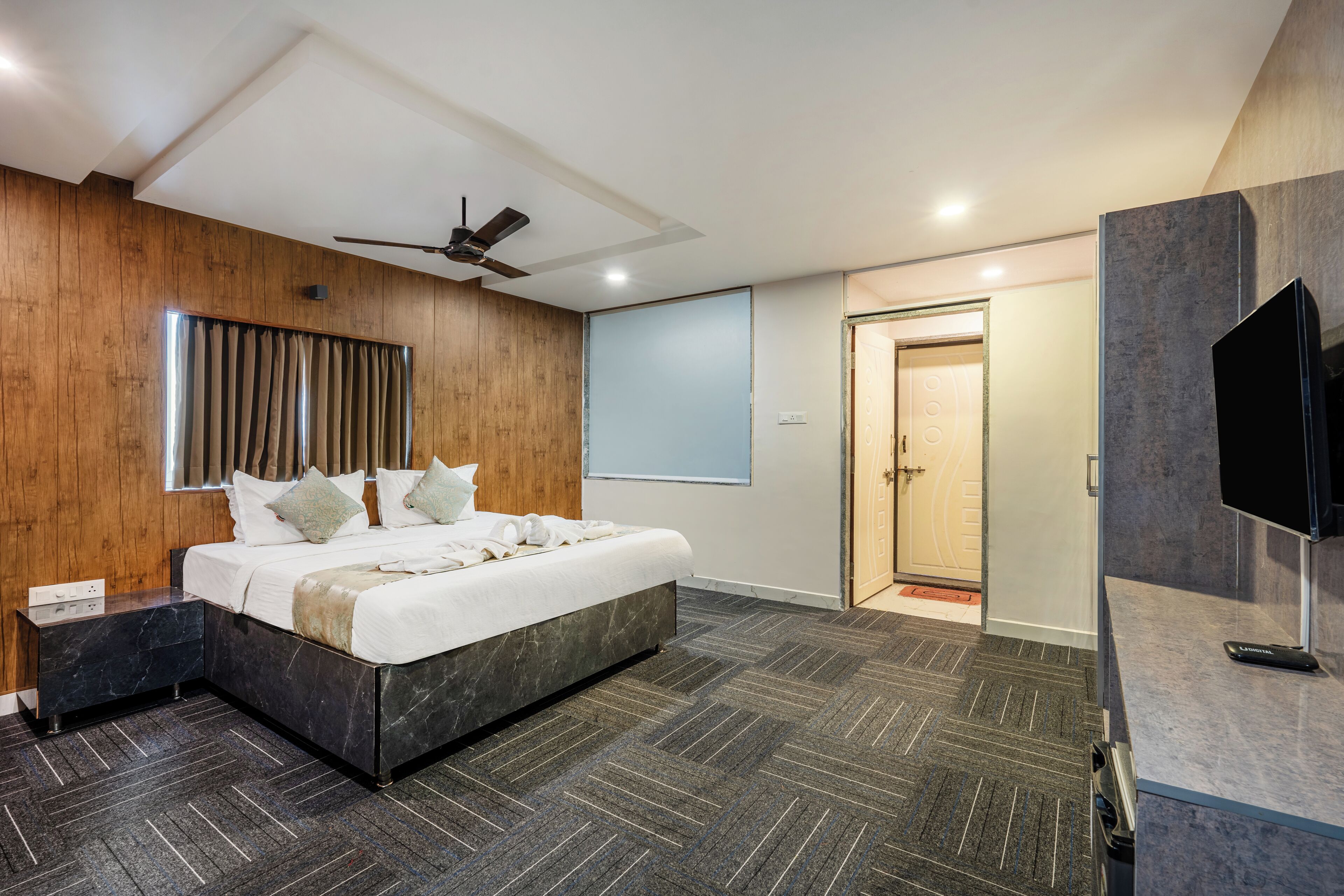Une chambre moderne avec un grand lit, des murs recouverts de panneaux en bois, un ventilateur de plafond et un téléviseur.