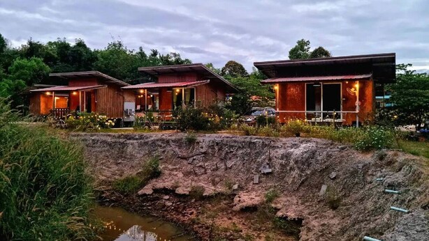 Un hotel de estilo rústico tipo cabaña, con tres edificios de madera, cada uno con un porche e iluminación exterior. Un pequeño arroyo corre frente a la propiedad.