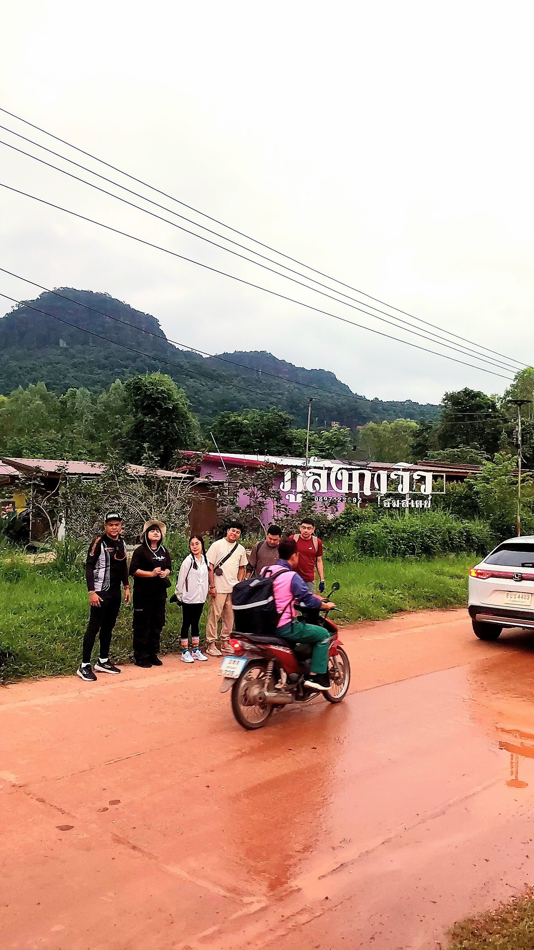 A group of people standing on a road with a motorcycle in the foreground.