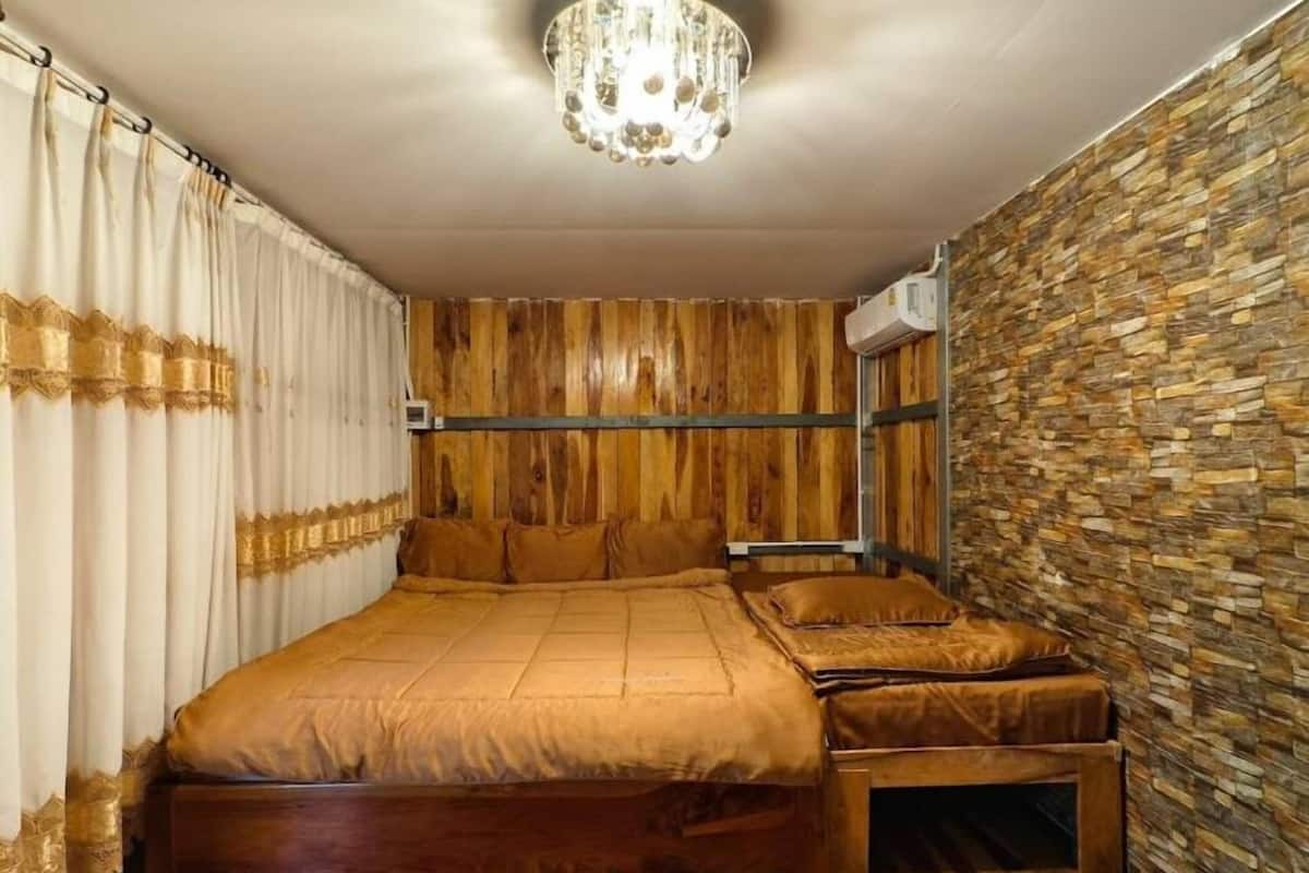 Quarto com cabeceira de madeira, cama com colcha marrom, mesa de cabeceira e lustre.